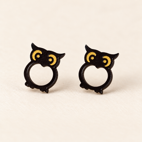 Dark brown owl stud earrings with yellow eye details, an inward-pointed opening and asymmetric feet, studio pair