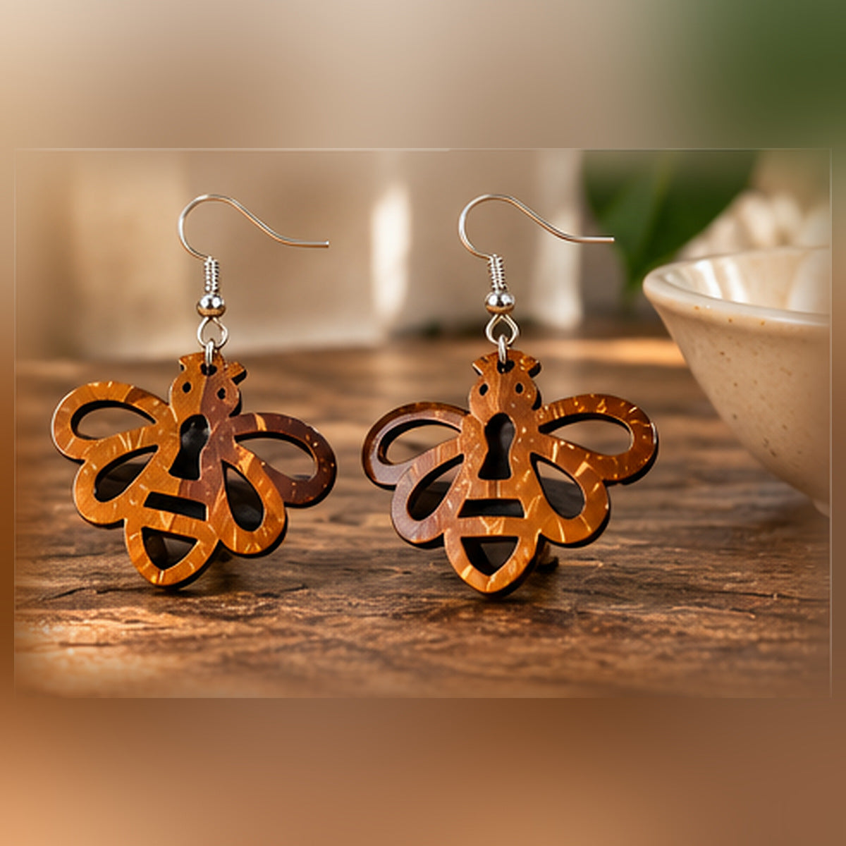 Brown openwork bee dangle earrings photographed on natural wooden surface