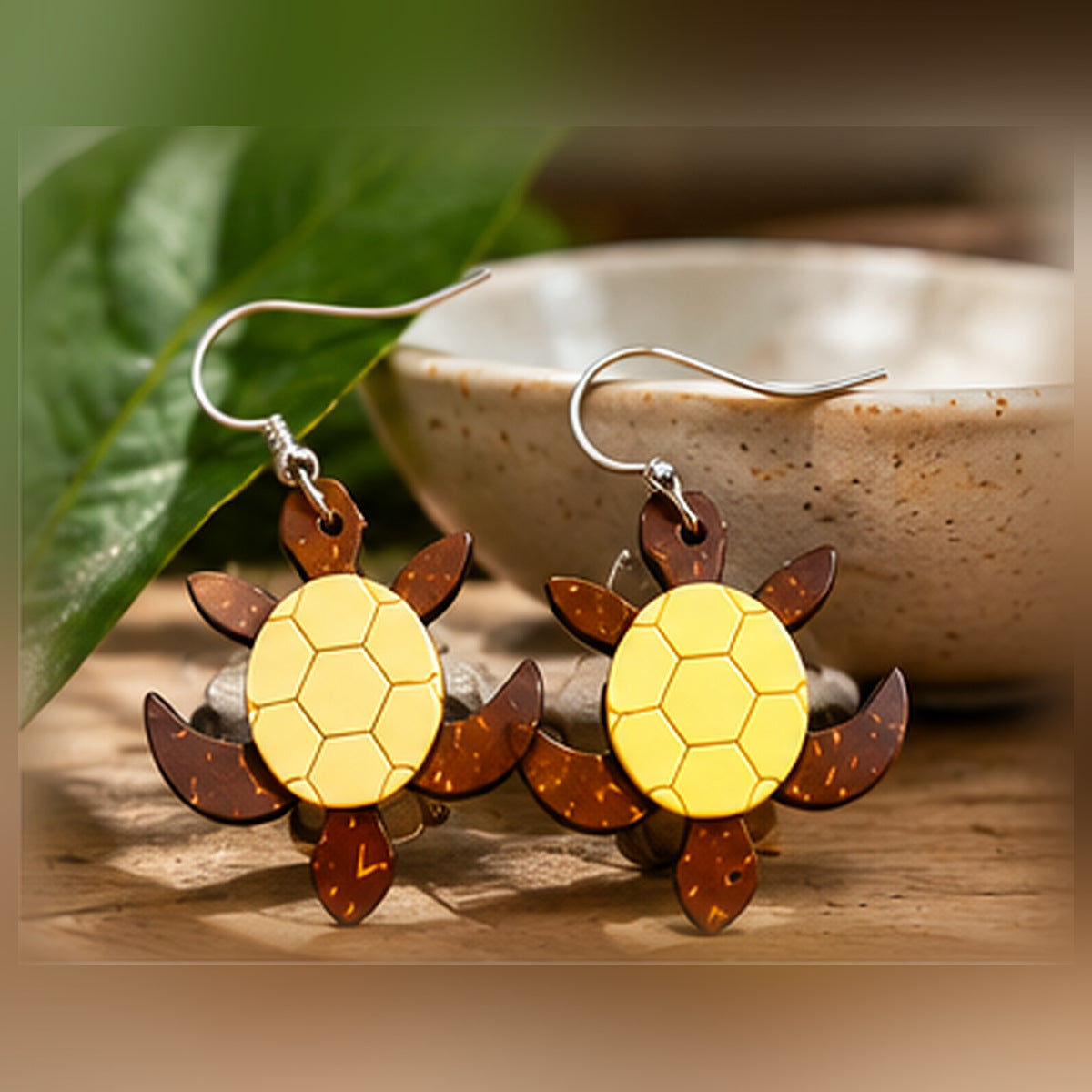 Pair of yellow and brown sea turtle earrings styled with ceramic bowl and leaves