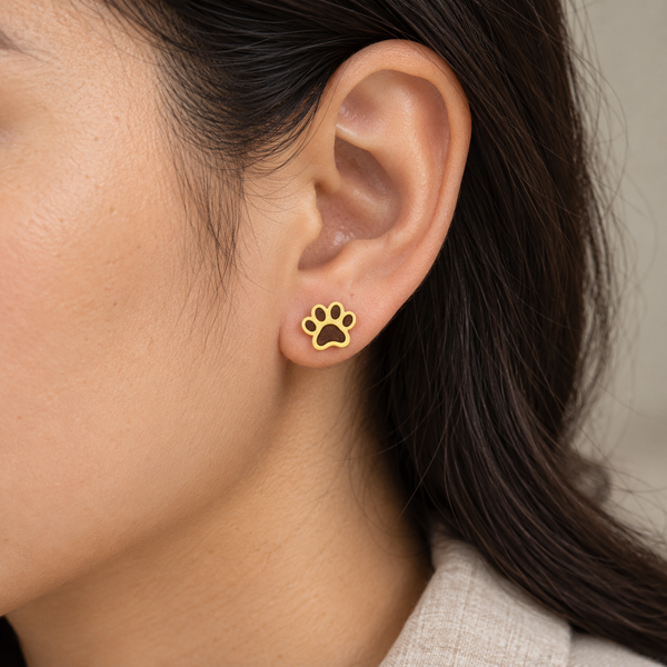 Yellow paw print stud earrings with solid dark brown filled pads, worn by an adult woman